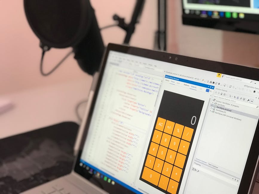 A silver laptop with a black keyboard is placed open on a light wooden table, displaying lines of code or text in a coding or text editing application on its screen. The laptop is positioned in a well